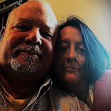 Sherry and Mike sitting close together indoors, sharing a quiet, affectionate moment. Mike has a white beard and bald head, while Sherry leans in with long dark hair.